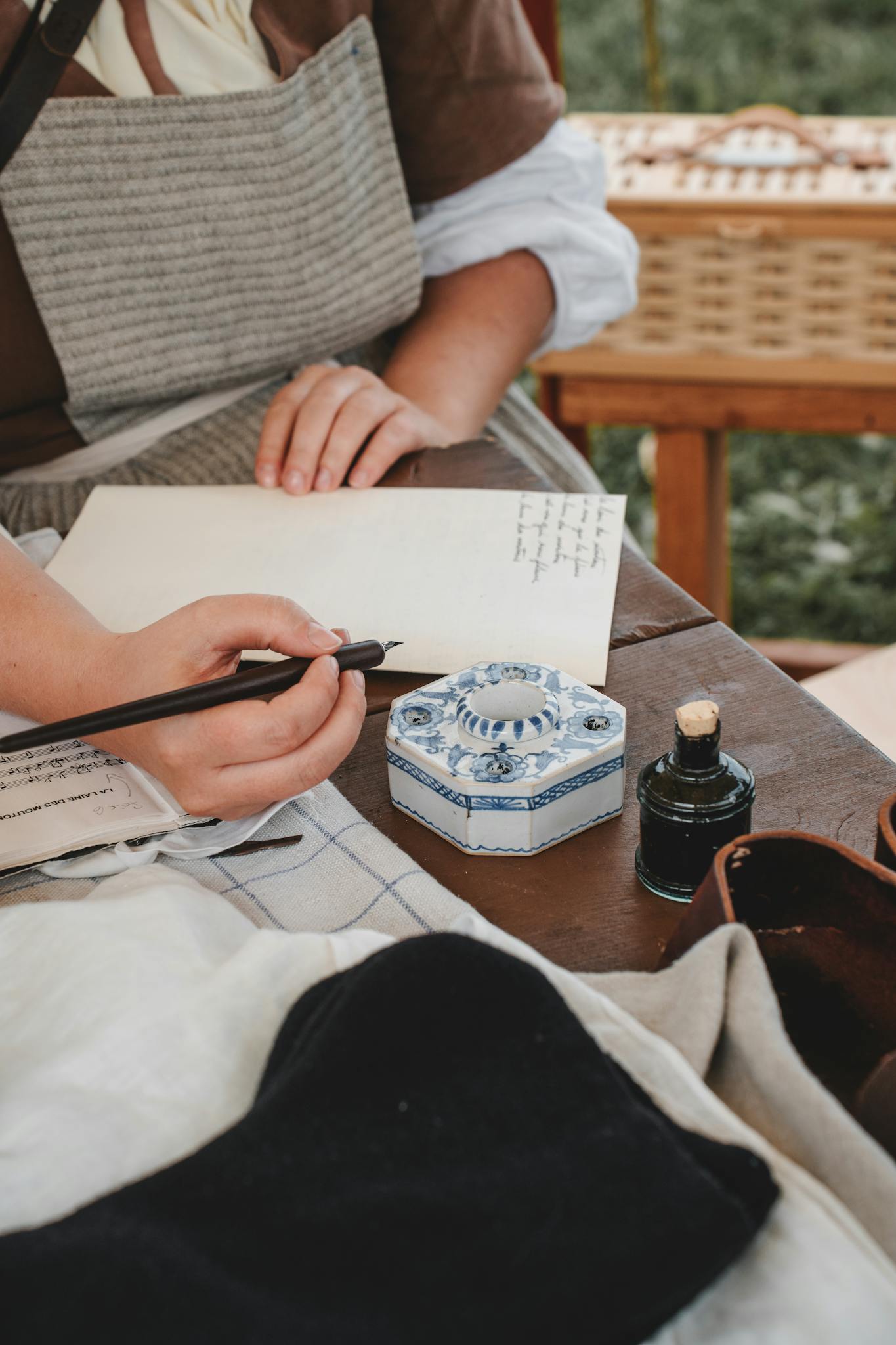 A woman writes a letter using a traditional ink pen and inkwell, evoking an 18th-century atmosphere.