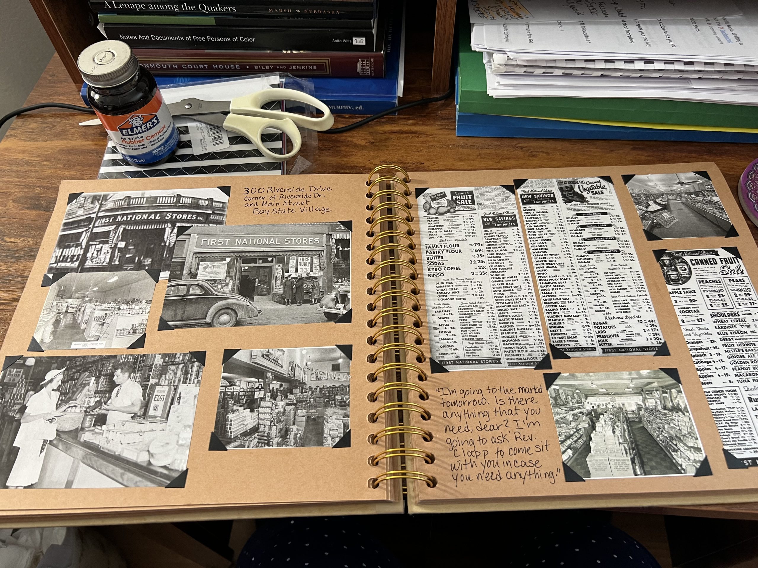 A desk workspace showing a scrapbook of historical research, vintage photos, and newspaper clippings for a novel project.